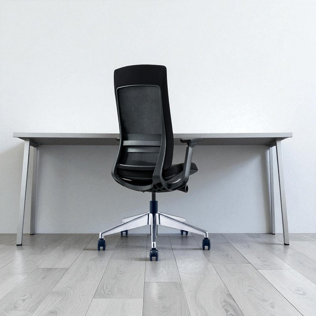 Black office chair in front of a white desk against a white wall.