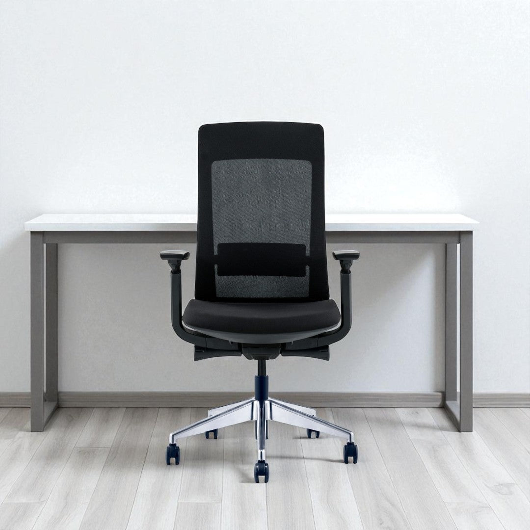 Black office chair in front of a white desk against a white wall.
