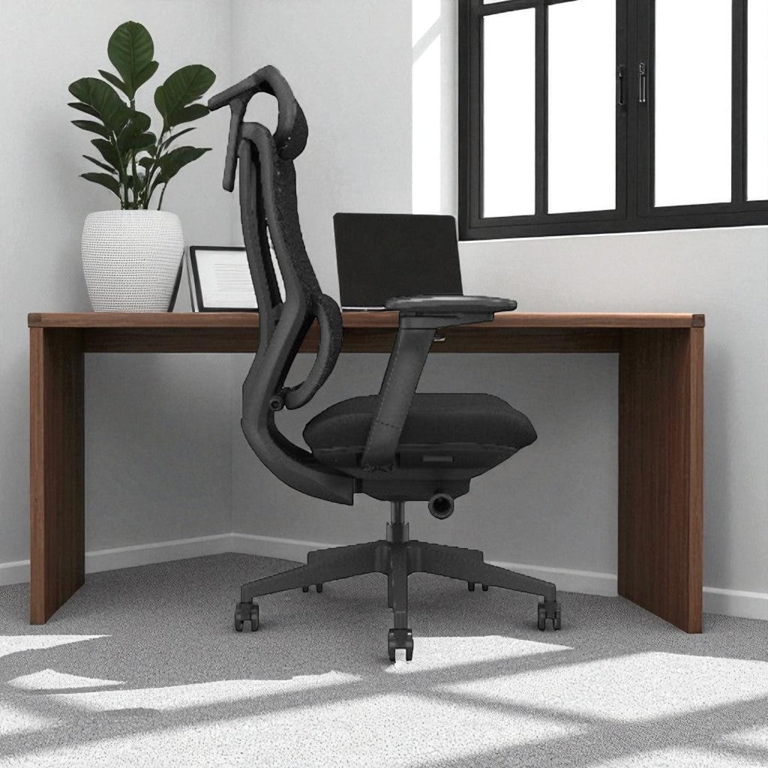 Black office chair in front of a wooden desk with a laptop, plant, and picture frame in a room.