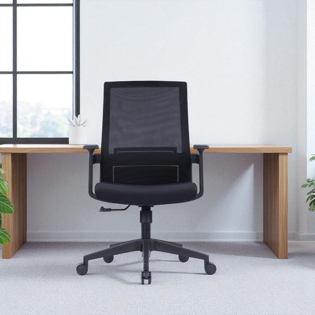 Black office chair in front of a wooden desk with a light gray wall and window in the background.